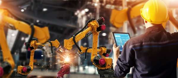 Industrial engineer with tablet managing robotic manufacturing line in Ghana; automated plant workforce outsourcing.